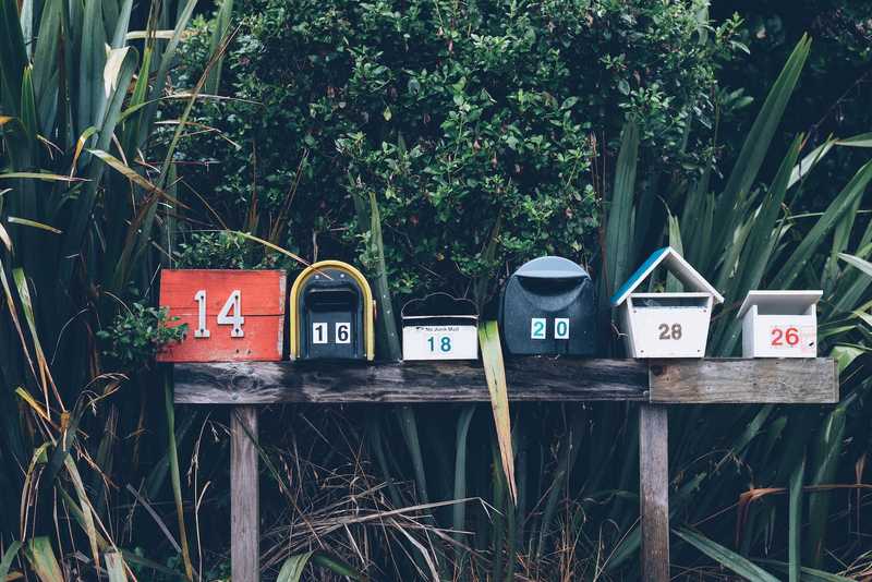 A row of six mailboxes in front of a bush